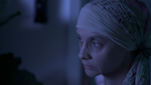 Close profile of a woman in a headscarf, lit in cool blue.