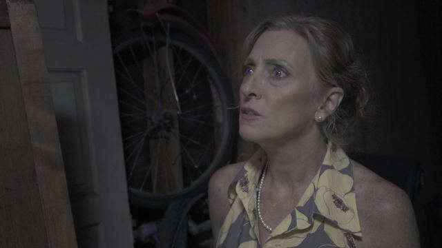 A frightened woman looks up in a dark storage room.
