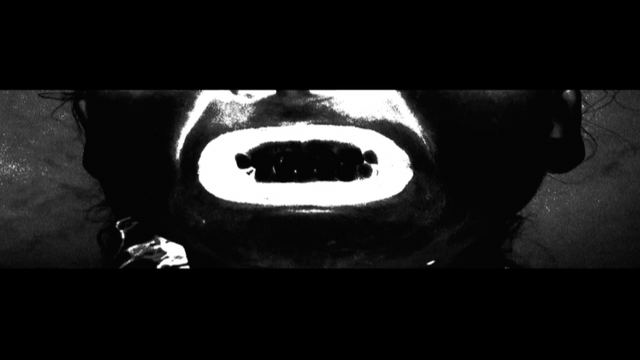 A screaming mouth in stark high-contrast black and white, letterboxed.