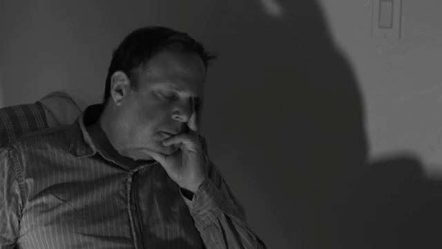A man deep in thought, hand at his chin, his shadow on the wall.