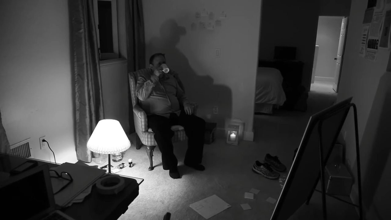 Eureka: a man sits alone in an armchair in a dim room lit by a single lamp, his shadow large on the wall beside an investigation board.